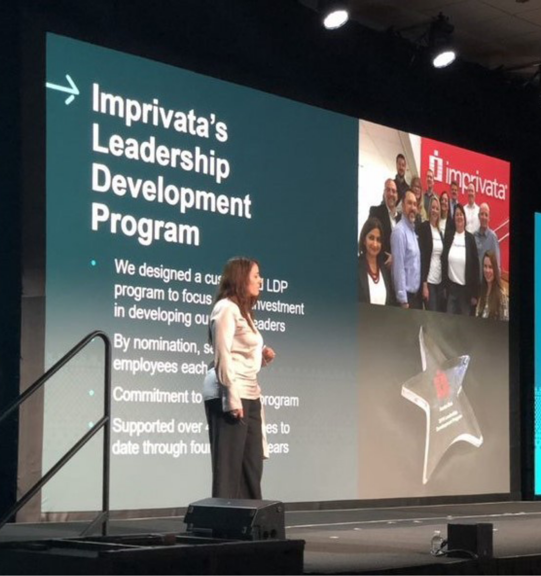 Image of an employee giving a presentation with slides on Imprivata's leadership development program behind her