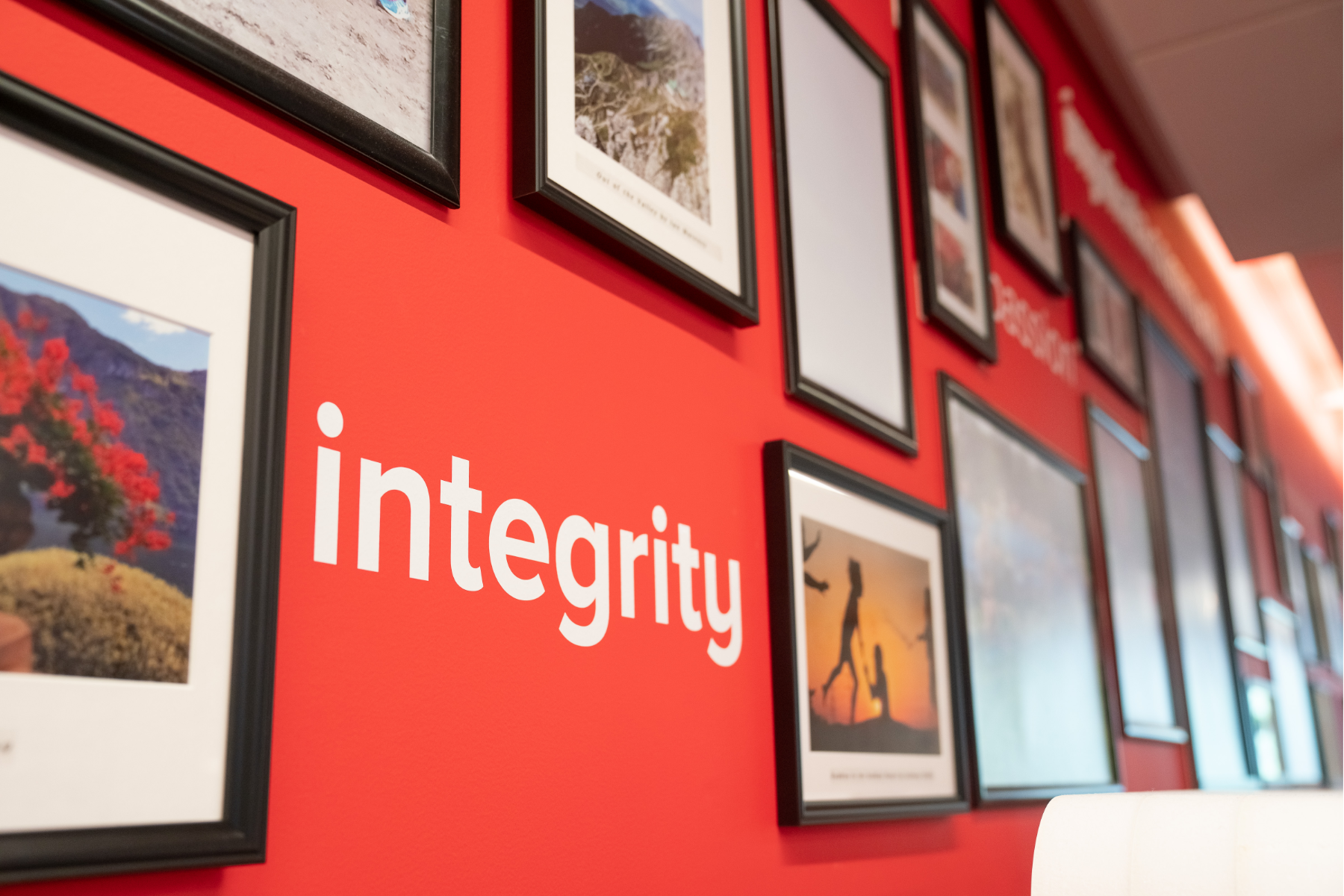 Image of a wall with the word 'integrity' painted on it surrounded by several framed photographs 