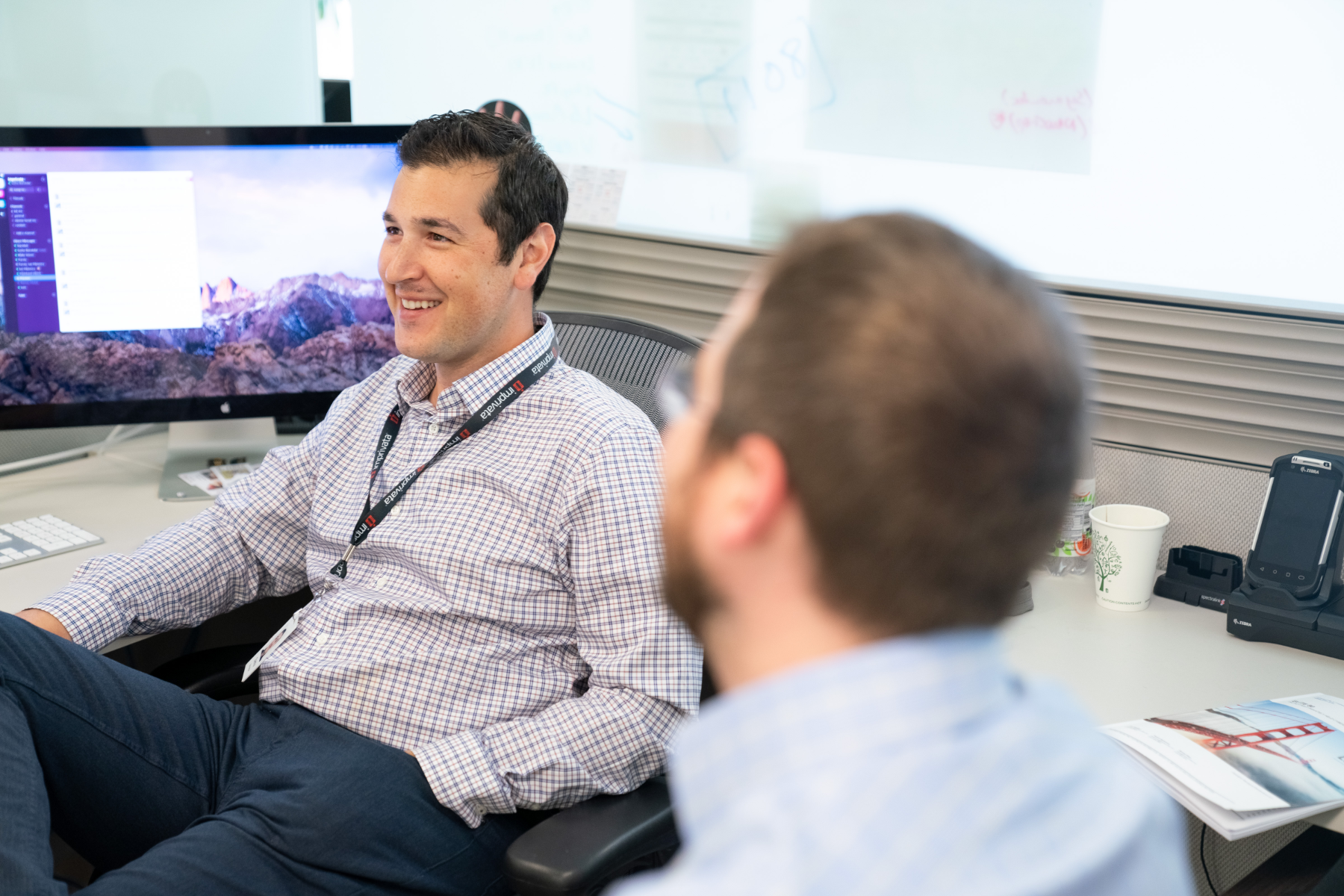 Image of two employees sitting in a cubicle smiling