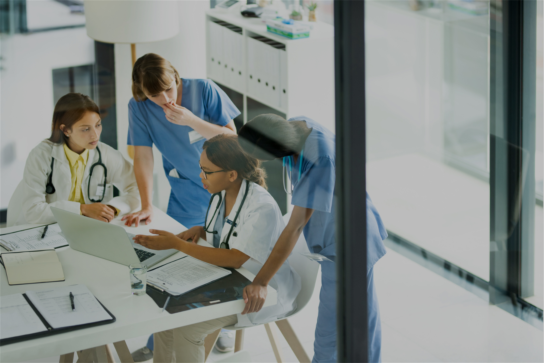 Image of a group of medical staff gathered around a table with a laptop on it