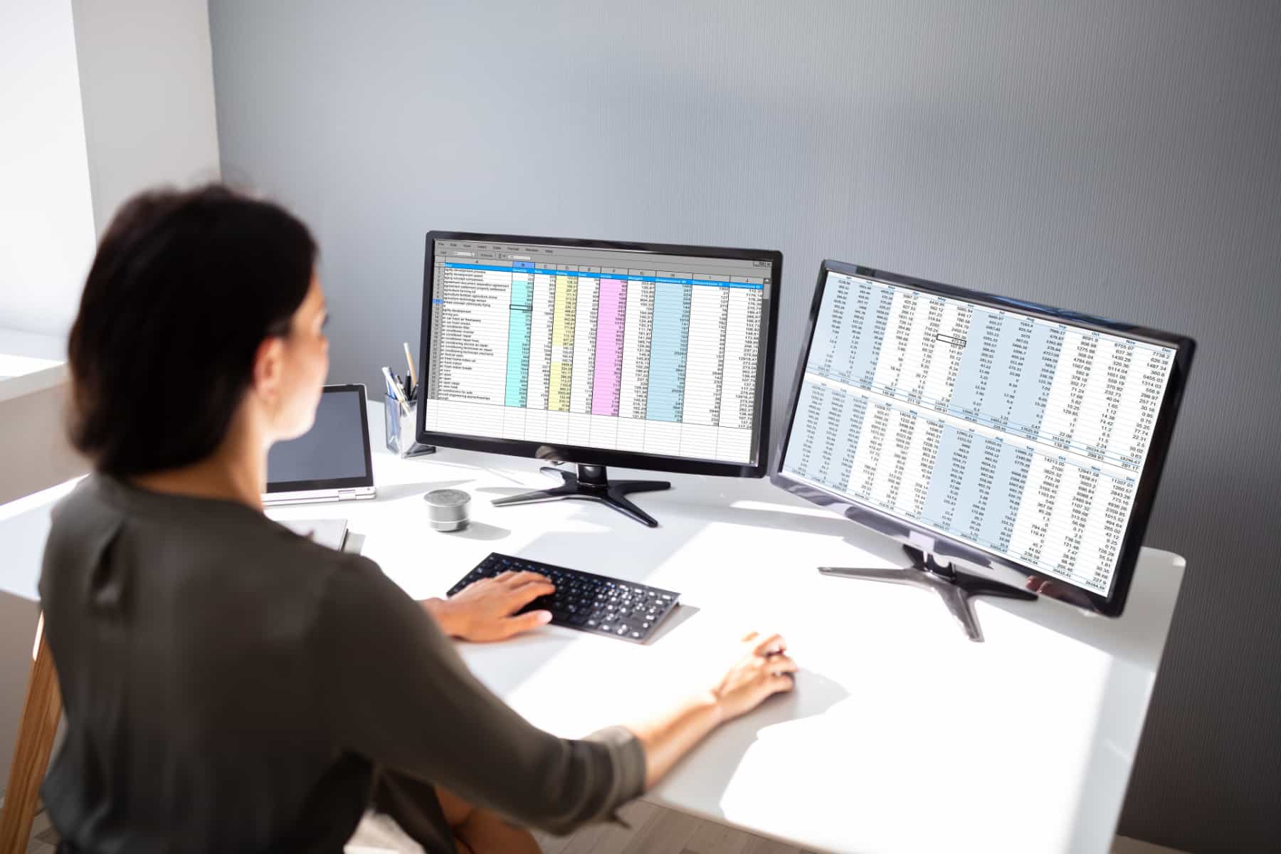 Image of a woman looking at spreadsheets on two desktop monitors