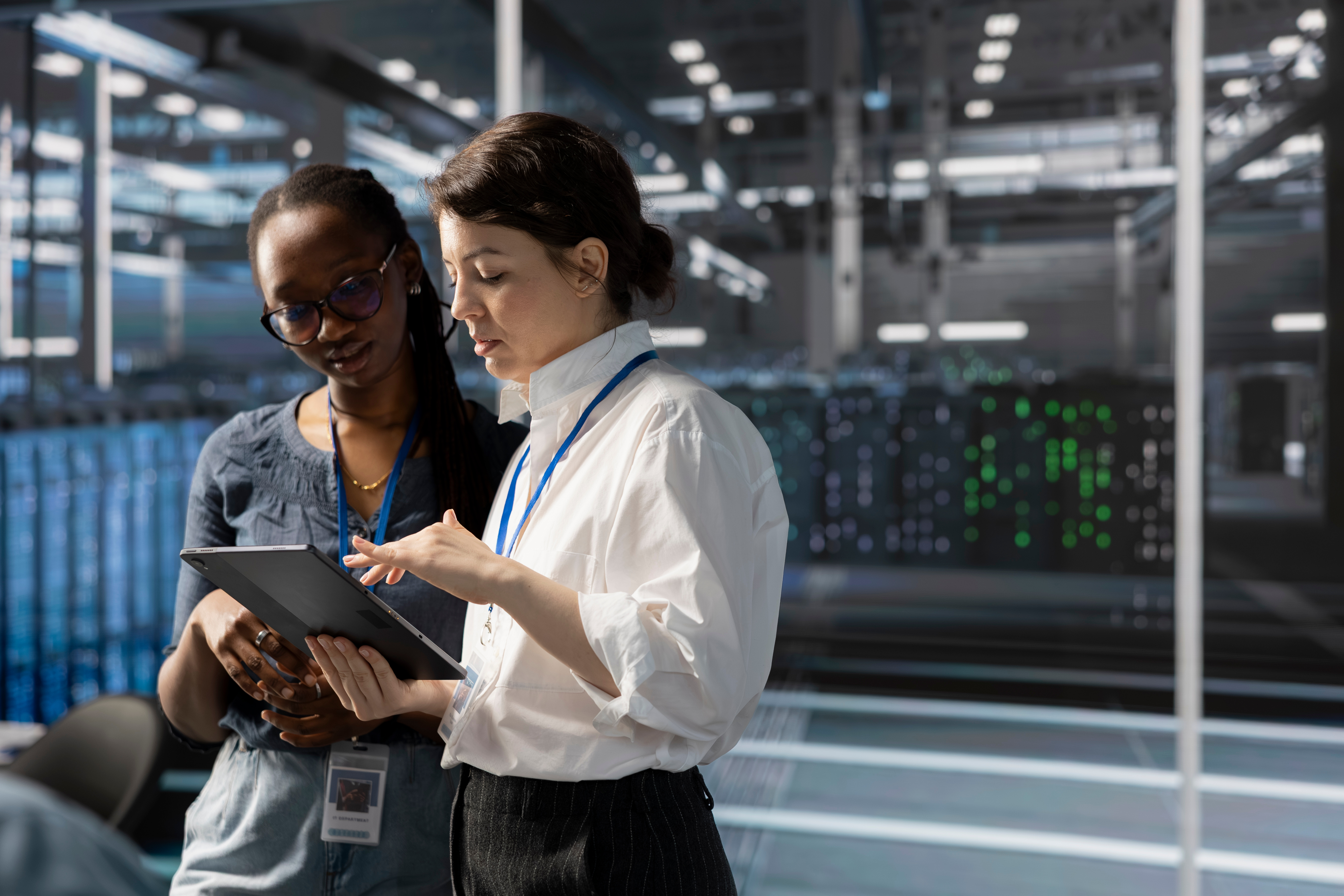 Photo of two people discussing work in a server room looking at a tablet