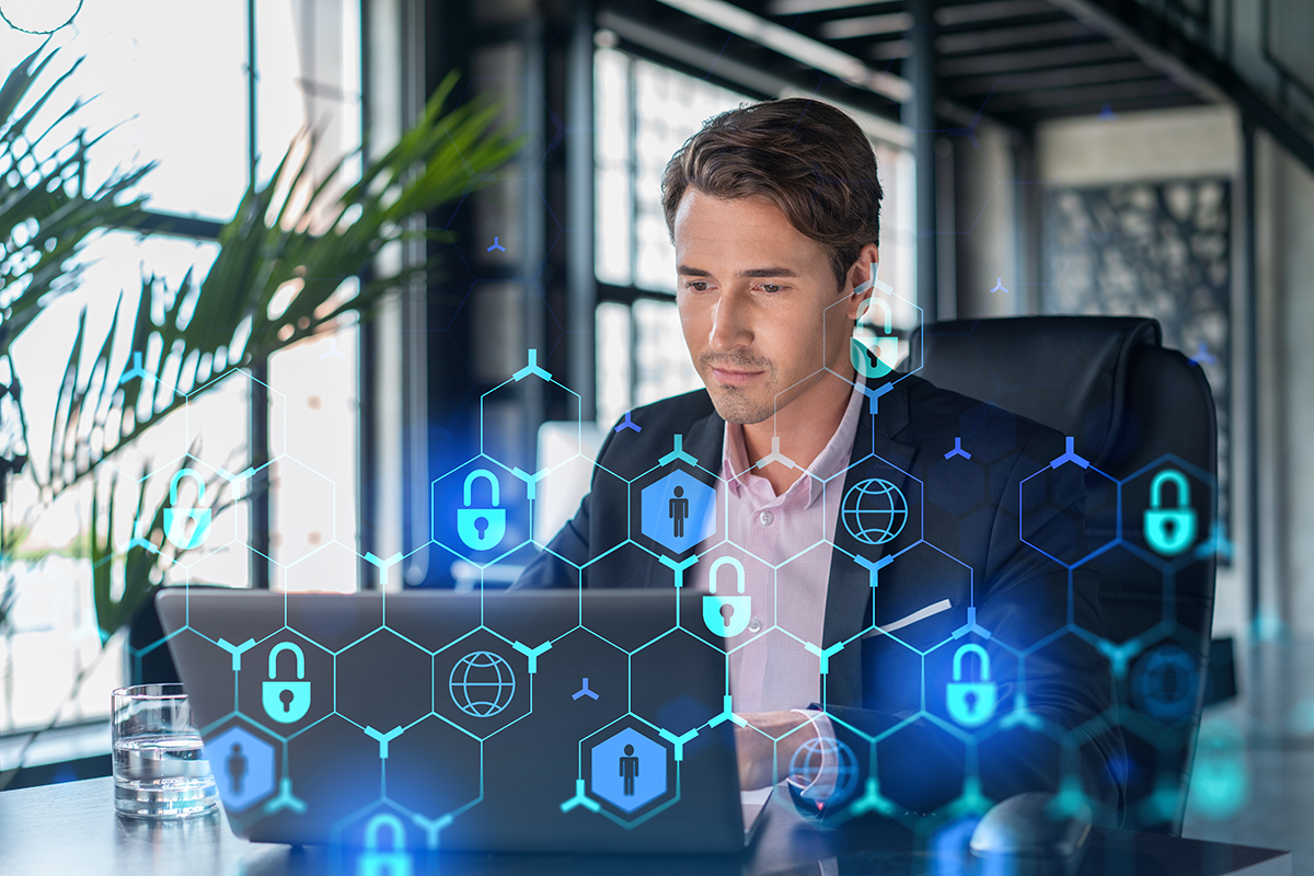 Remote access software and cybersecurity depicted by employee working on a laptop in an office setting with padlock hologram over image.