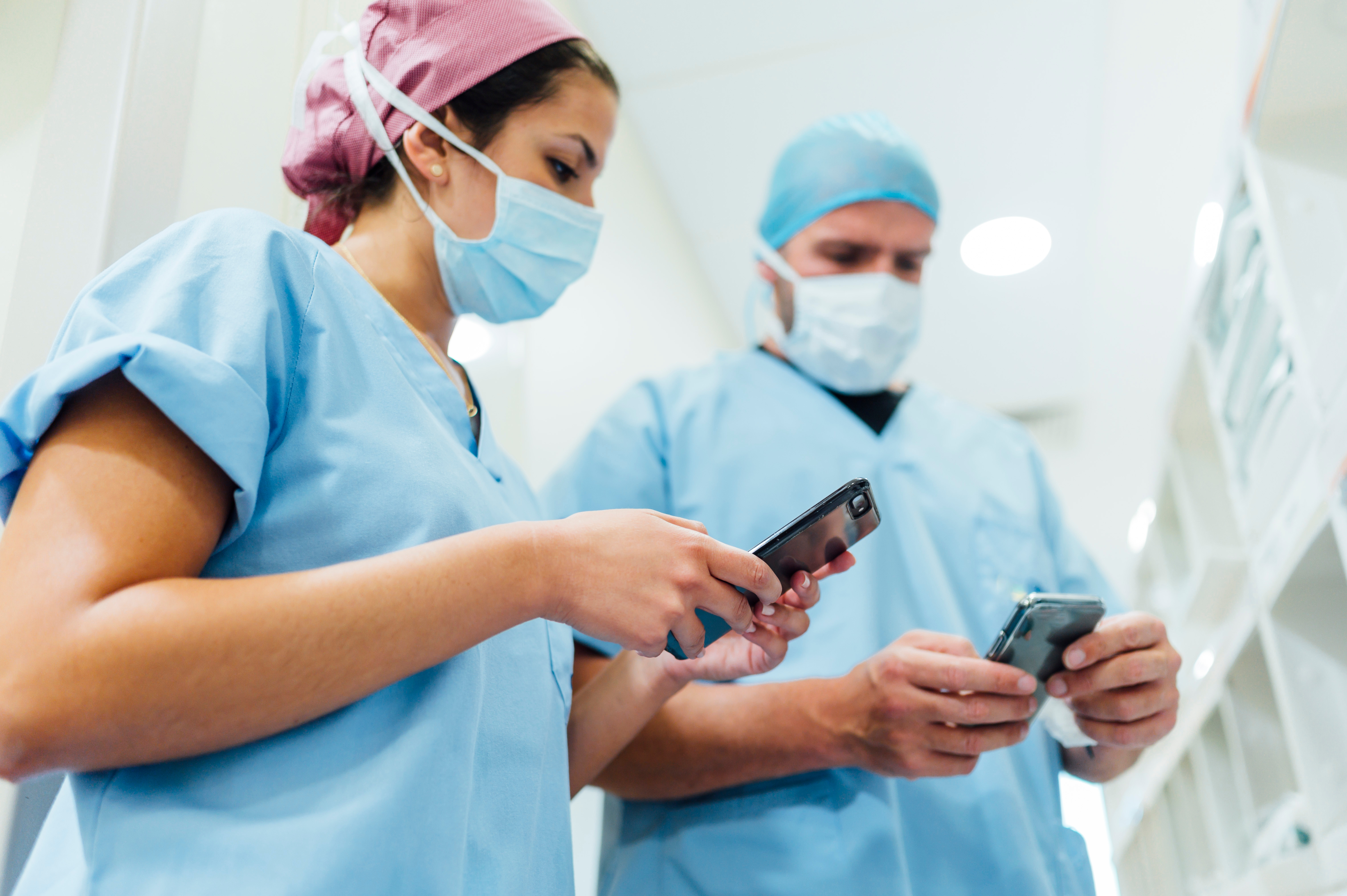 Two clinicians in scrubs using smartphones in a hospital