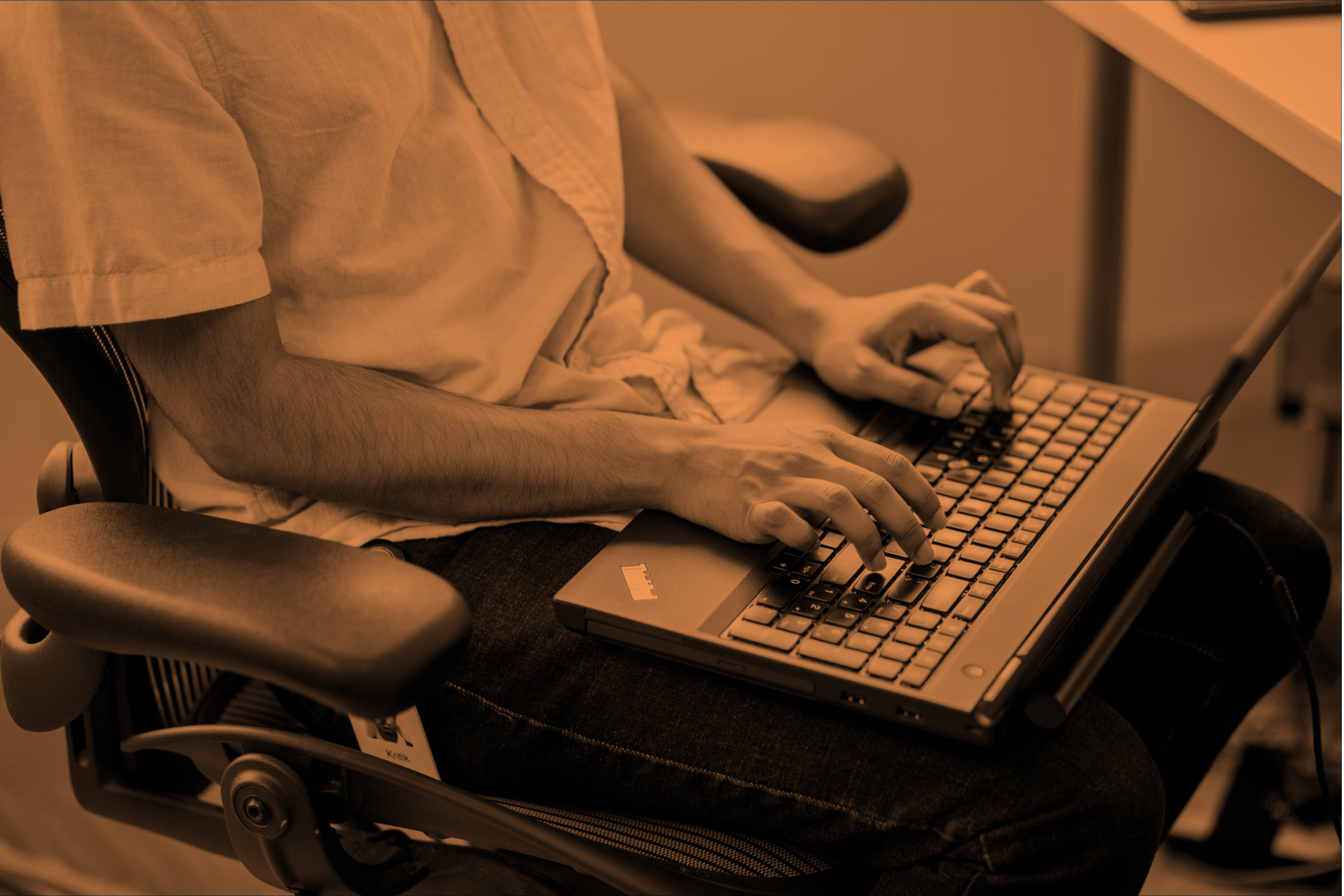 Image of a person in a desk chair typing on their laptop